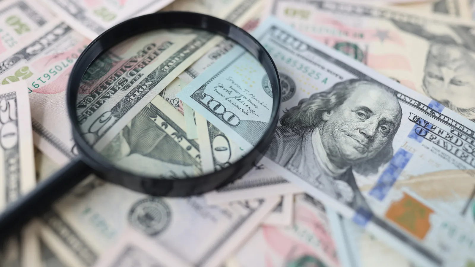 Magnifying glass laying on top of money because M&M Tax double checks tax returns for free.